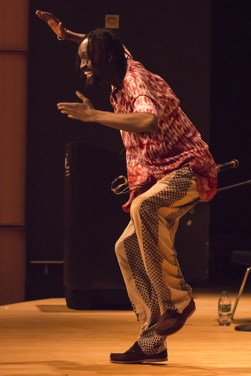 Maguette Camara, with a wide grins, performs with one leg hovering off the ground and one hand above his head